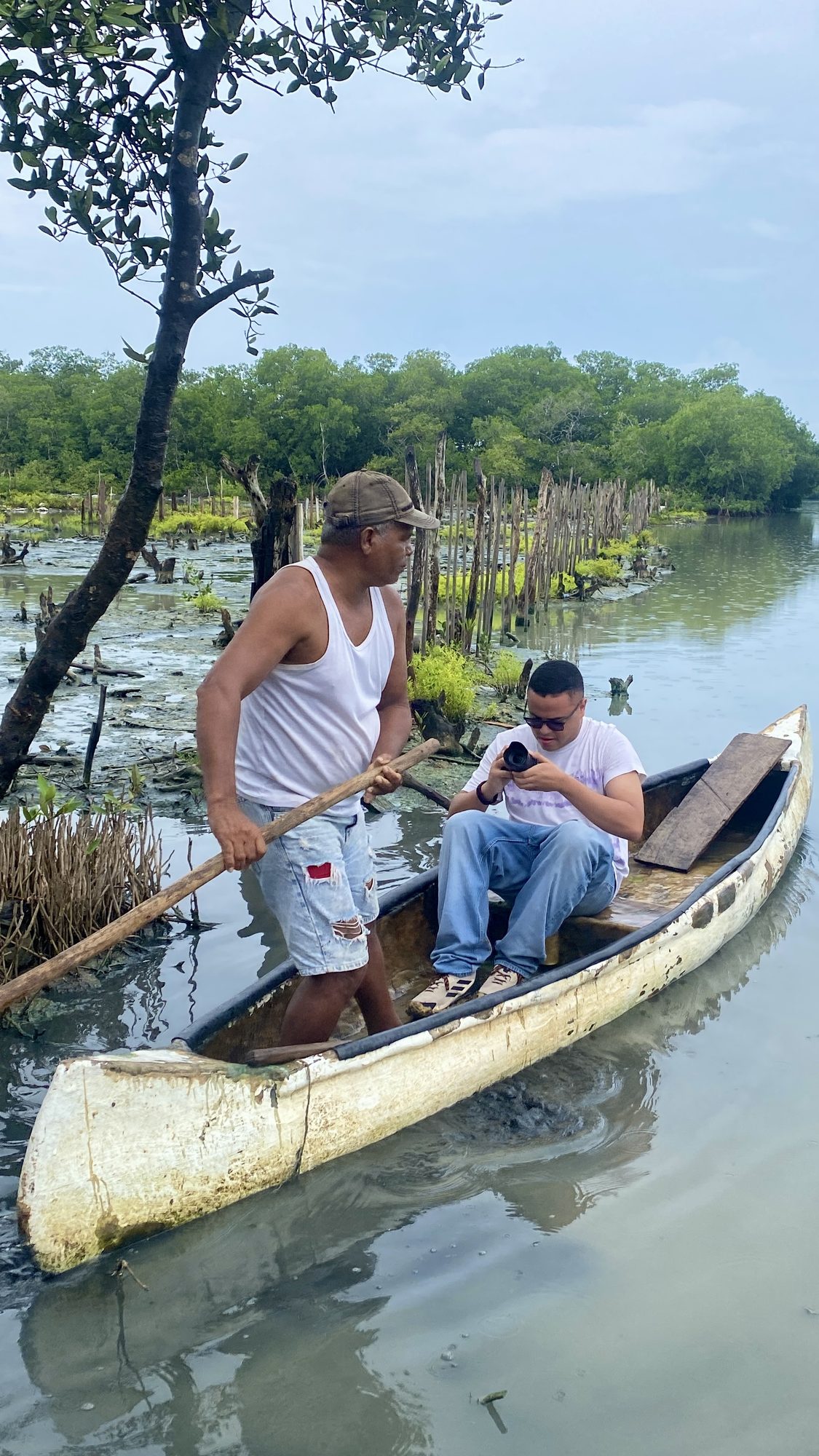 Camilo revisando la cámara a bordo de una canoa de madera en la ciénaga junto a un pescador