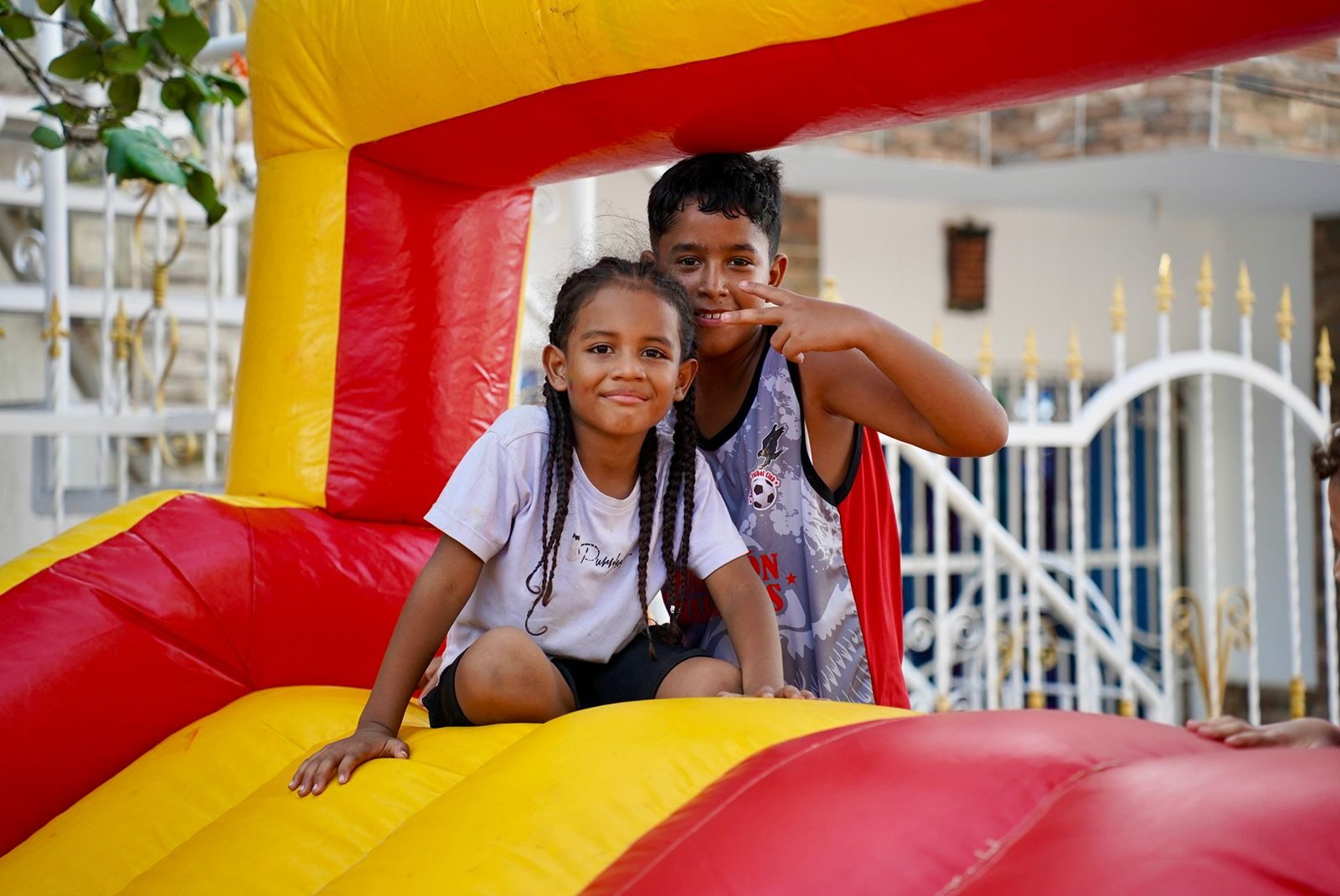 Dos niños posando sobre un inflable rojo y amarillo, el niño hace la señal de paz
