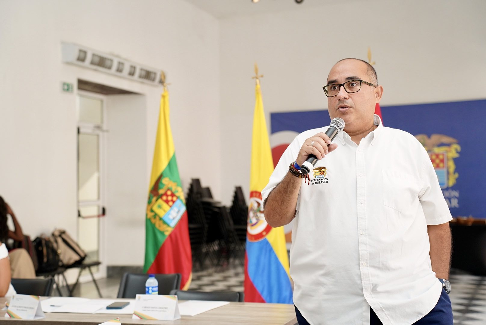 Funcionario hablando por micrófono junto a las banderas de Colombia y Bolívar