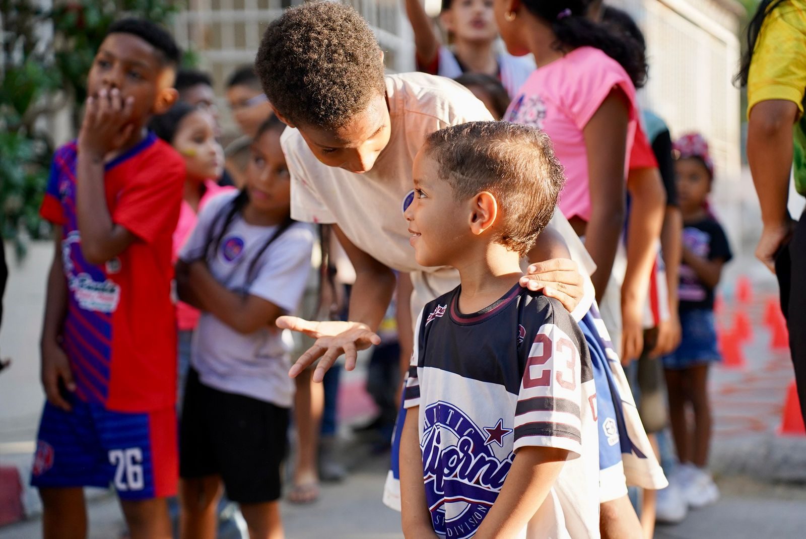 Adolescente conversando con un niño más pequeño rodeados de otros niños en la calle