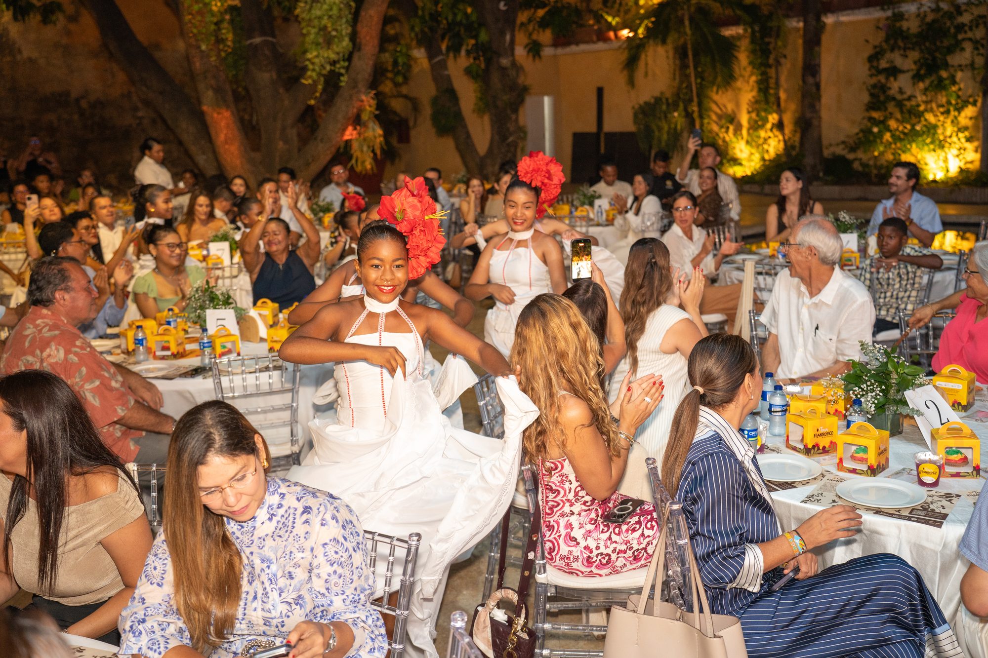 Cena al aire libre con bailarinas tradicionales y asistentes aplaudiendo en el Tour Filantrópico